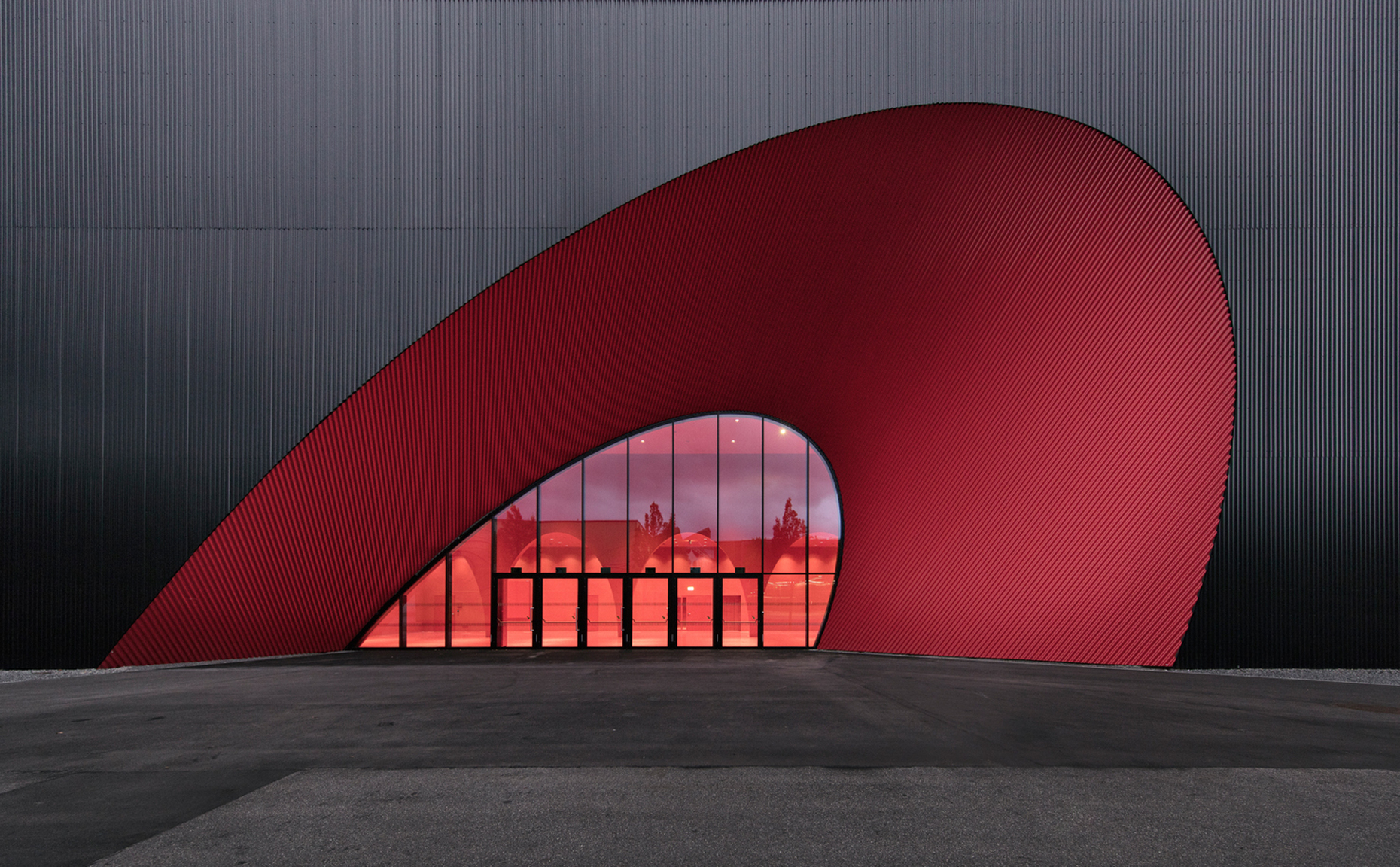 The conical section in its intense crimson red, the “trade-fair red” of Messe Dornbirn, creates a zestful contrast to the rectangular building’s black exterior.