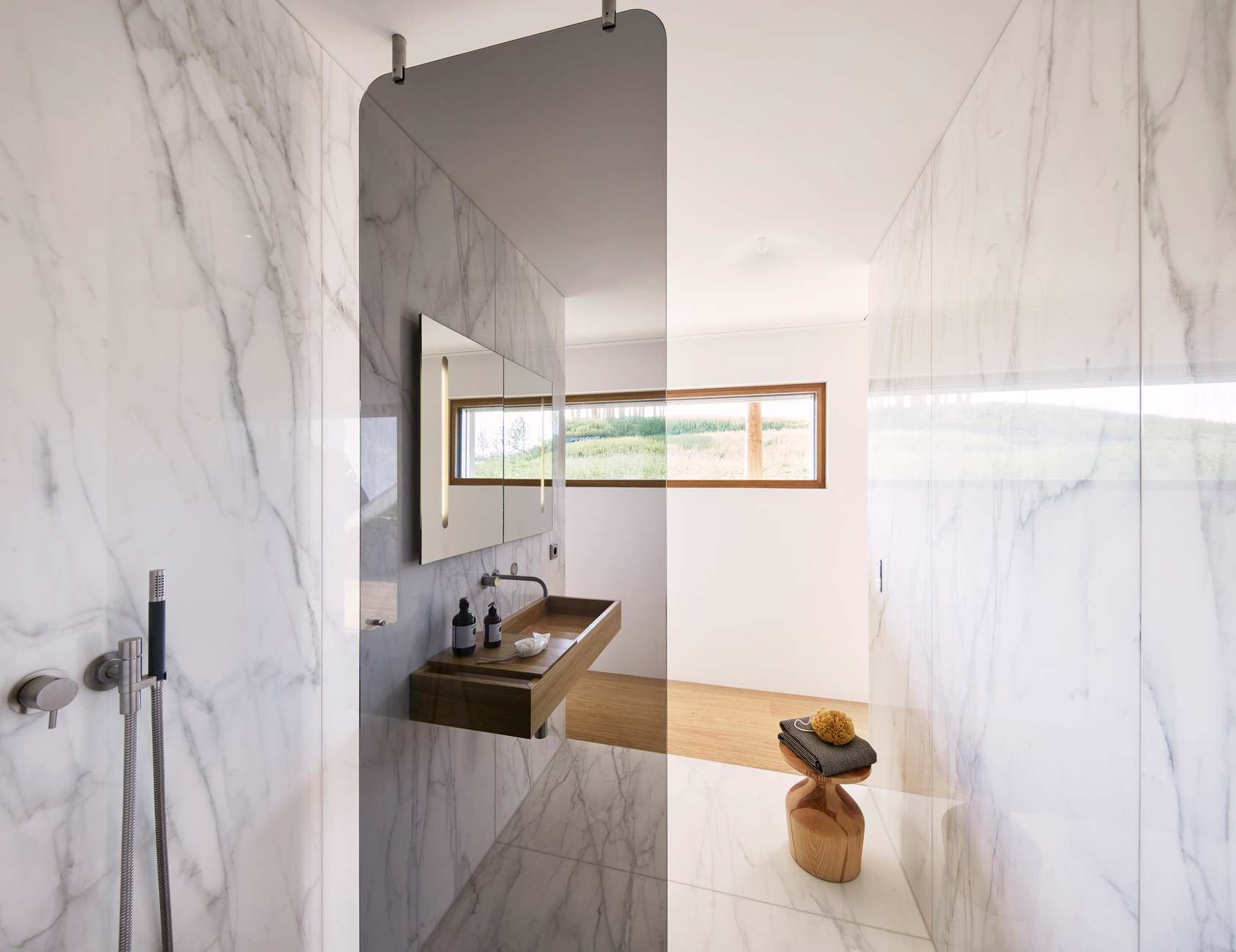 Vom Boden losgelöste Glasabtrennungen dienen als Spritzschutz und sanfte Abtrennung zum Raum. Allein der Materialwechsel von Parkett zu Marmor verdeutlicht die jeweilige Nutzung.